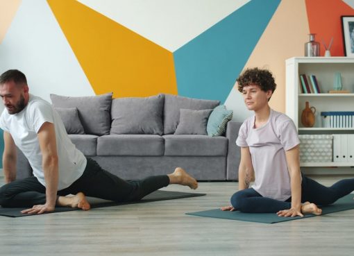Young couple man and woman are doing yoga at home exercising together on mats practising asanas in apartment moving simultaneously. Youth and sports concept.